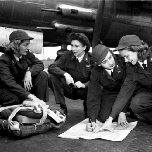 Women Airforce Service Pilots reviewing a flight map beside a military aircraft during World War II
